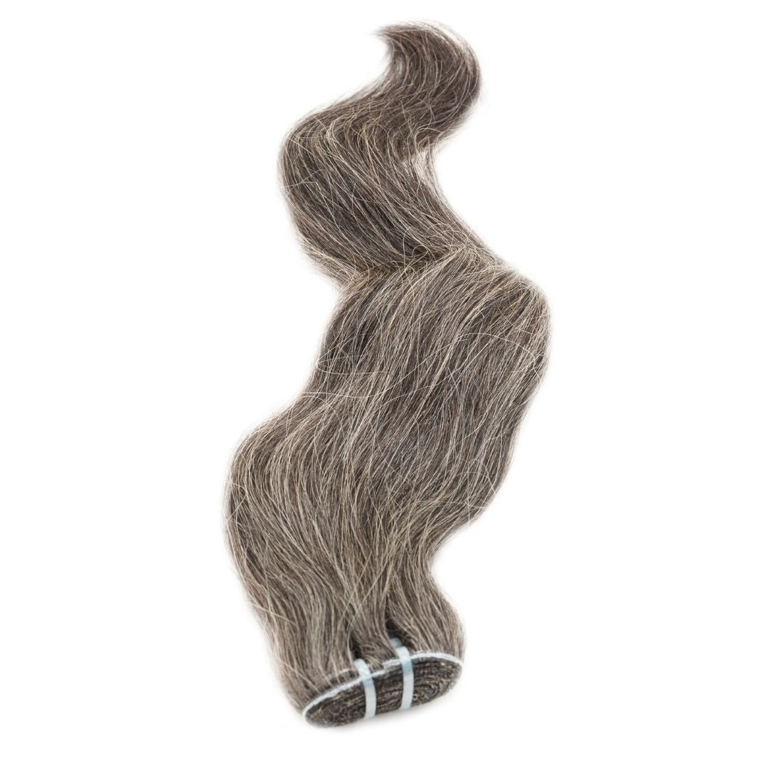 A bundle of hairdiamondz's Vietnamese Natural Gray Hair Extensions, showcasing 100% natural alternating gray and darker shades, is elegantly bound with blue ties against a white backdrop. This double drawn collection highlights a soft, flowing texture with a wavy, salt-and-pepper sophistication.